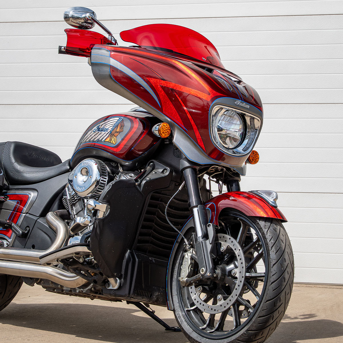 A red and black Indian Chieftain PowerPlus motorcycle photographed outdoors against a white garage door, with the front wheel and fairing prominently visible.