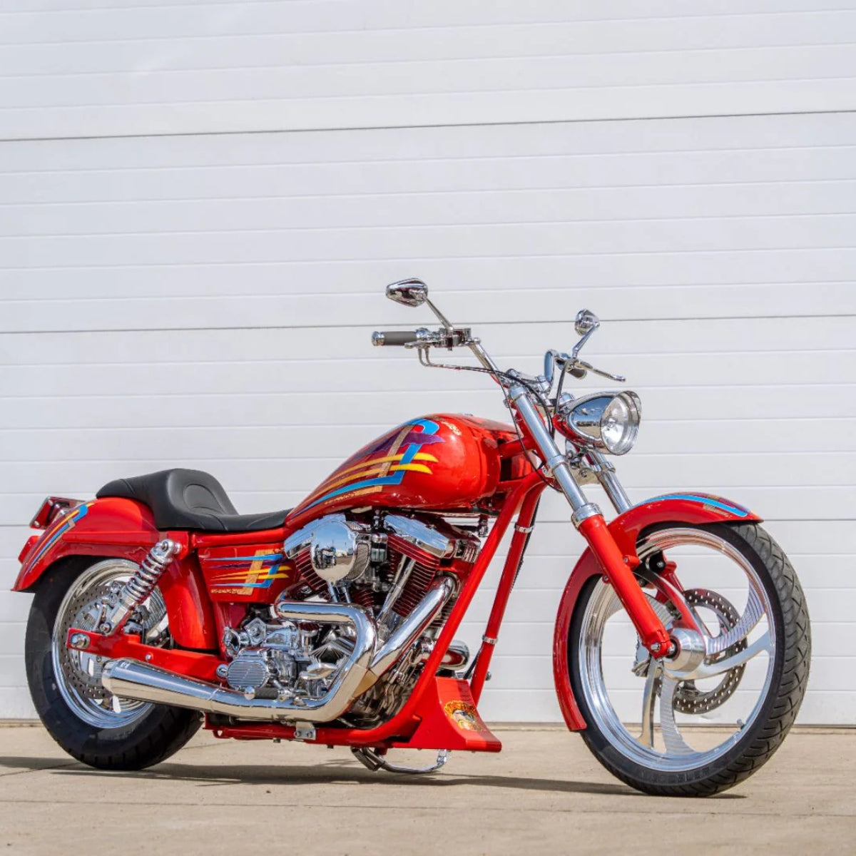 Picture of a custom built Dyna outside on a sunny day in front of a garage door.