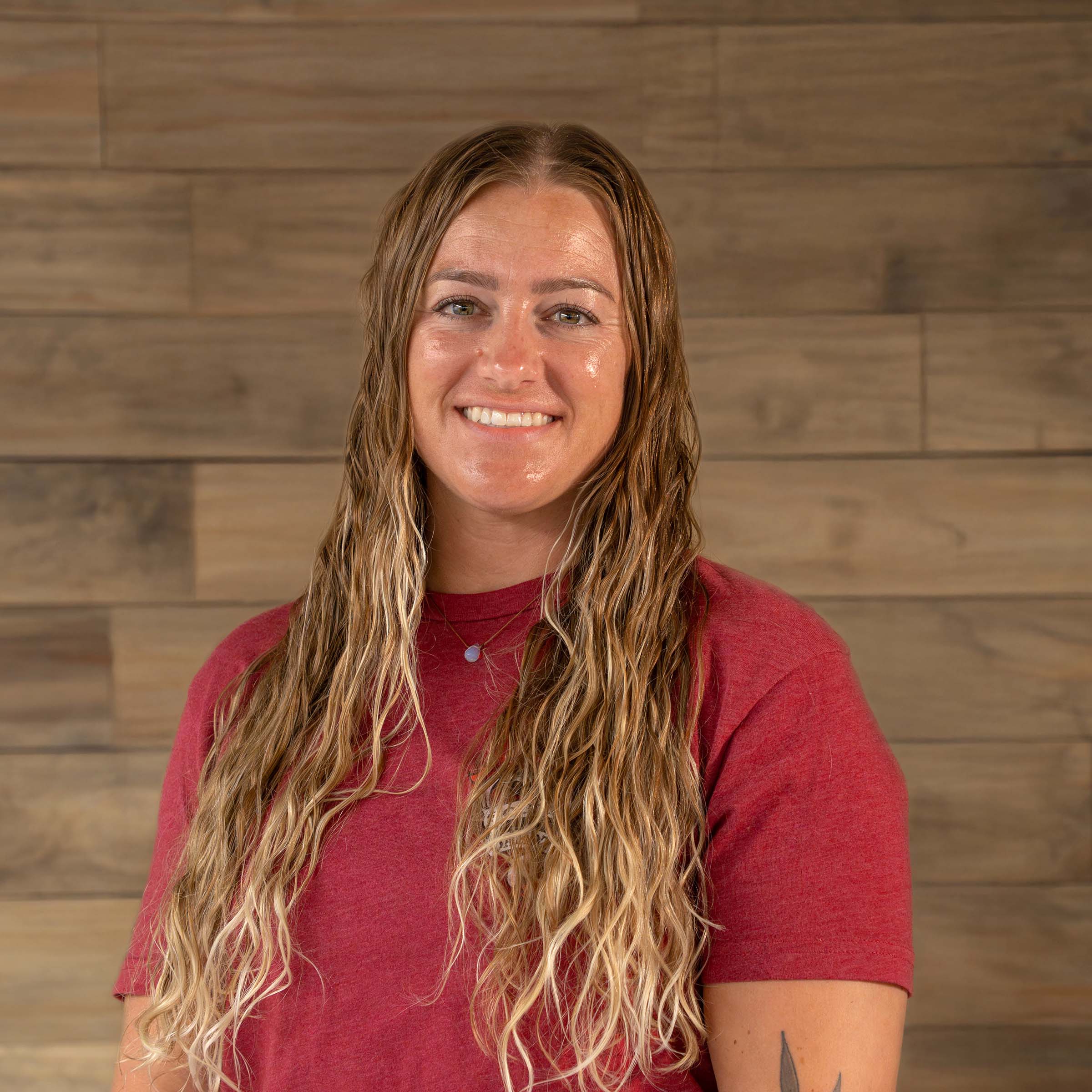 Emily Bier of Mitchell South Dakota poses in front of a wooden wall for a Klock Werks employee headshot.