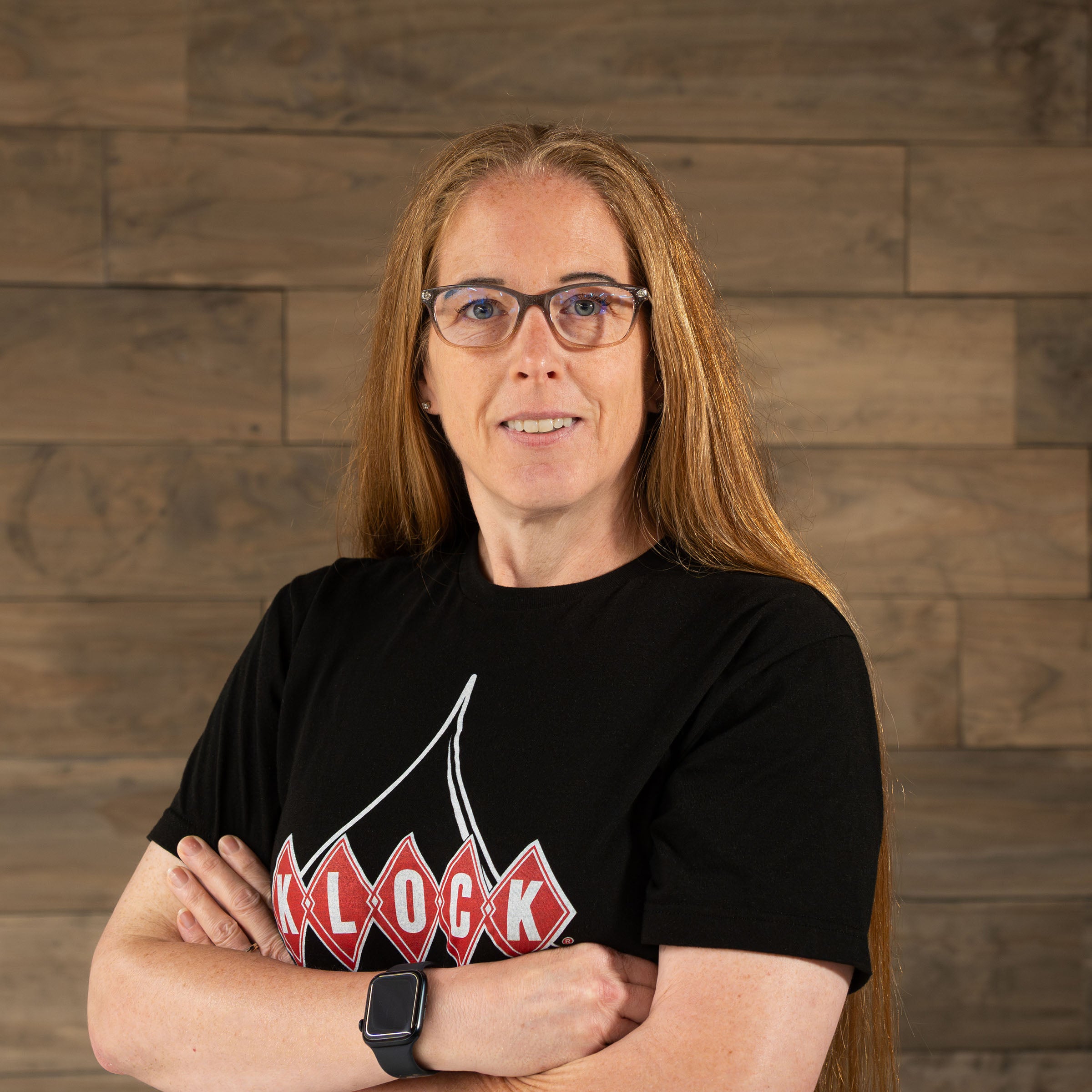 Klock Werks Employee Kristie Contreras standing against a wooden backdrop