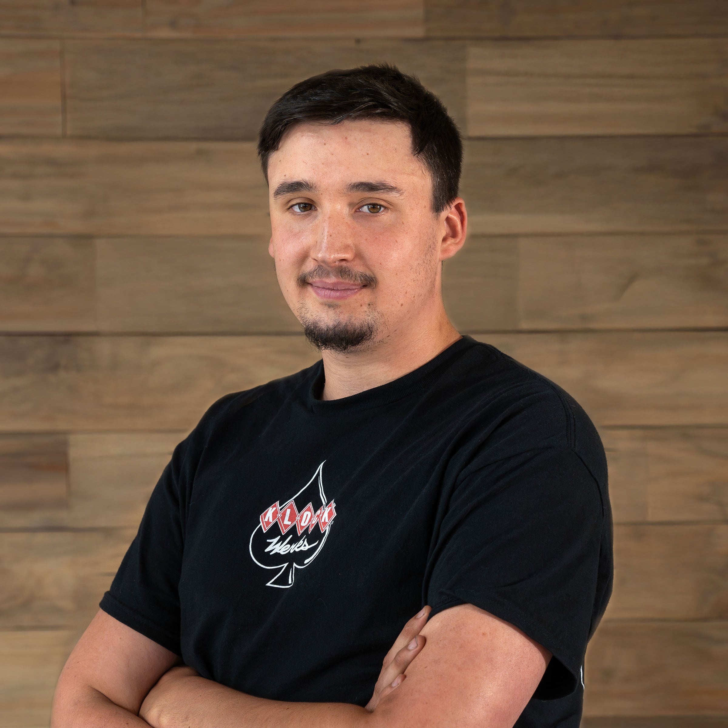 Richard downs of Klock Werks poses in front of a wooden backdrop for his employee photo.