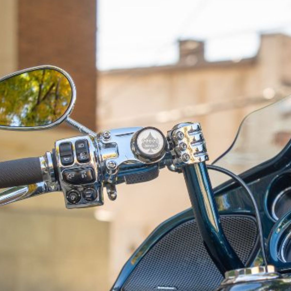 Close-up of a motorcycle handlebar with a phone mount, mirror and control buttons, blurred background